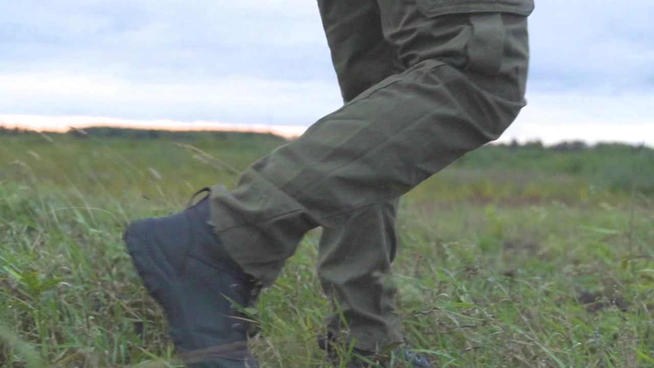 Toma de ángulo bajo de persona caminando sobre campo de hierba verde al aire libre con equipo de protección militar