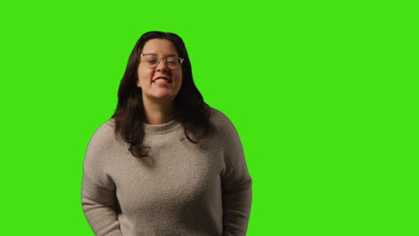 retrato de estudio de una mujer joven sonriente vestida casualmente con gafas de pie contra el fondo de la pantalla verde 1