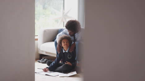 pre-teen boy sitting on the floor at home doing homework with his father sitting on the sofa behind him helping, looking at each other, seen from doorway
