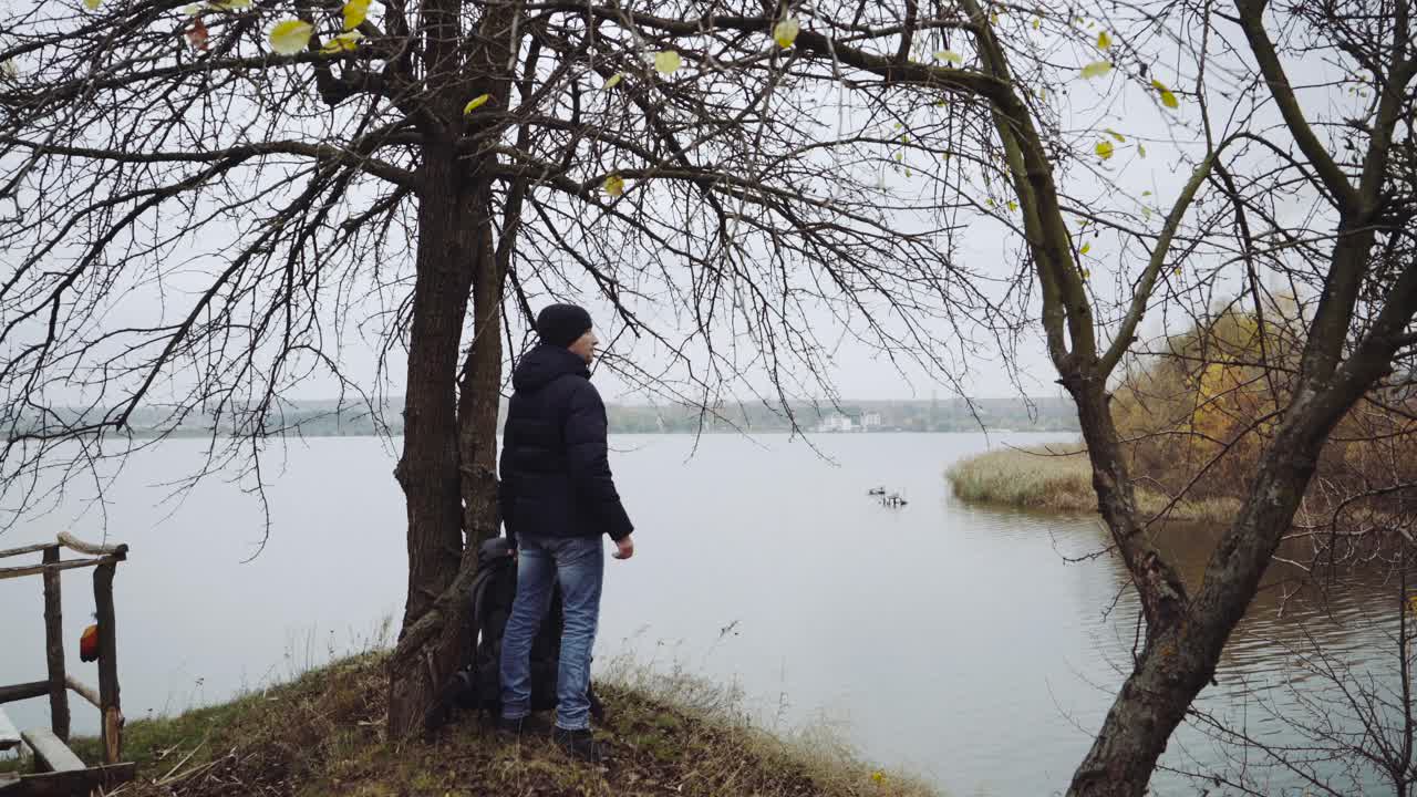 Man tourist standing near river. Back view of lonely man standing with backpack near river