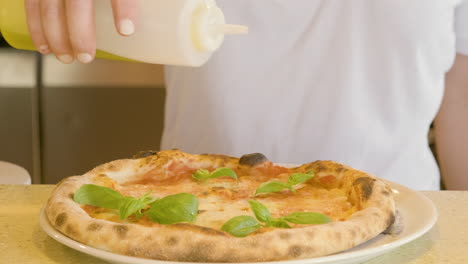 primer plano de un chef irreconocible que vierte aceite de oliva en una pizza margherita horneada