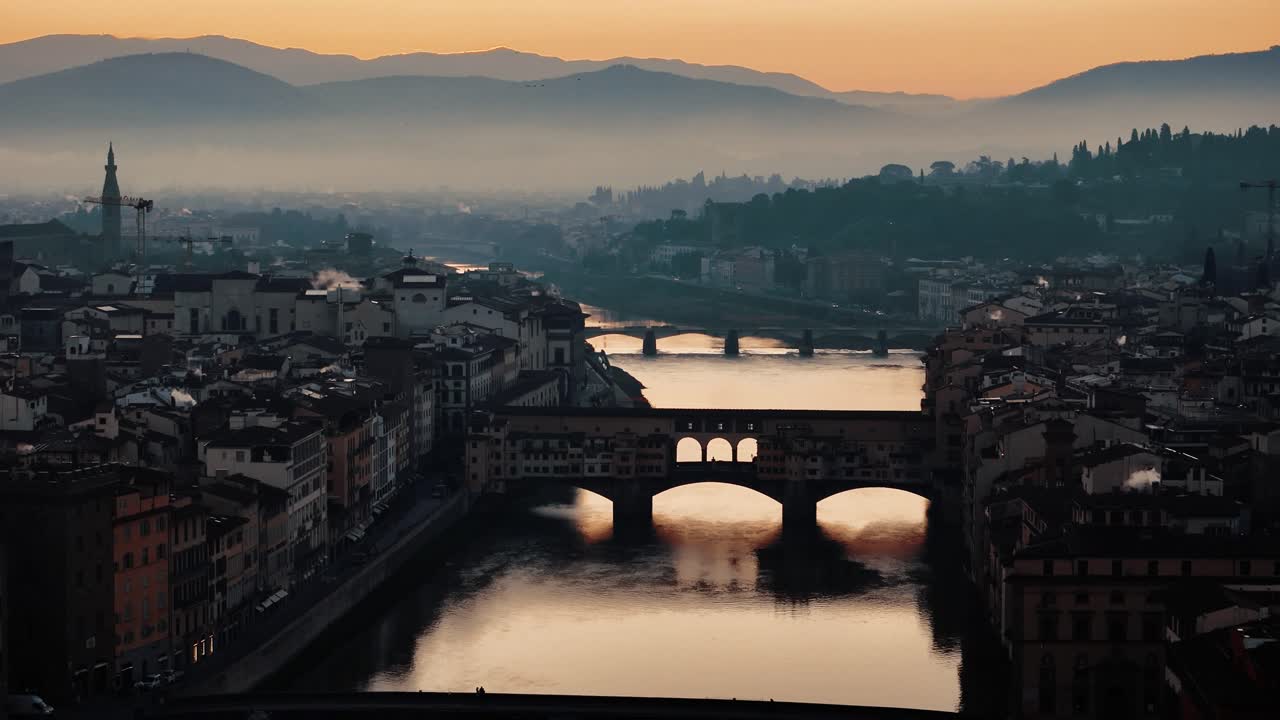 Slow approach over Ponte Vecchio with vibrant orange sunrise reflecting in river