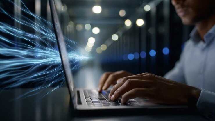 A focused individual works on a laptop in a high-tech environment, illuminated by blue light, symbolizing data transfer and advanced technology interaction