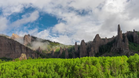 timelapse of clouds and fog above scenic rock formations and green forest. mill castle, crested butte, colorado usa