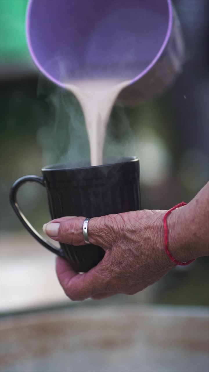 close up de leche de chocolate caliente que se vierte de un recipiente púrpura en una taza grande, con el vapor subiendo, sugiriendo una escena de cocina al aire libre