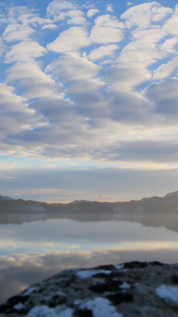 Video verticale: Telecamera in movimento che cattura nuvole gonfie che si riflettono su un lago di montagna con riva rocciosa