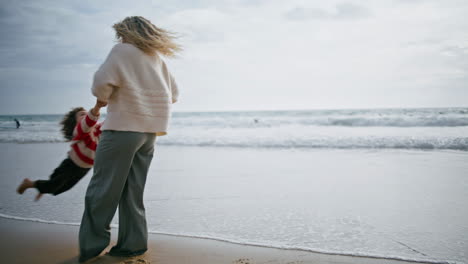 Madre-Alegre-Hijo-Girando-En-La-Orilla-Del-Océano.-Familia-Feliz-Jugando-En-La-Playa-Del-Océano