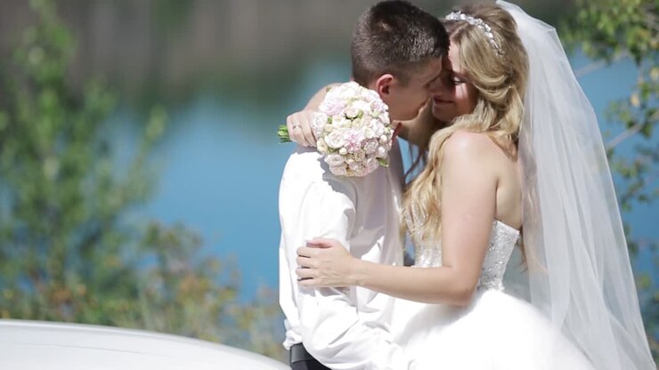 Bride And Groom By The River. Happy stylish bride and groom walking on the river, smiling and kissing