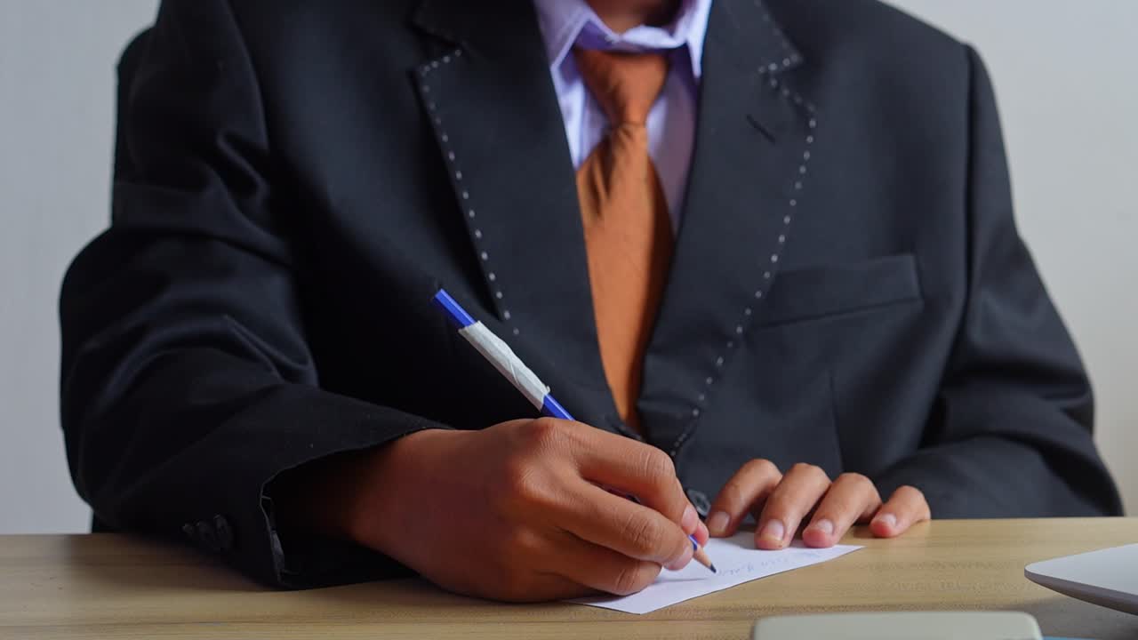 Businessman in suit writing notes on white paper with blue pen
