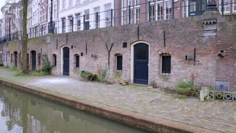 Utrecht-canals-showing-brickwork-wharfs-lined-with-trees-and-plants,-and-historic-wharf-cellars-with-blue-doors