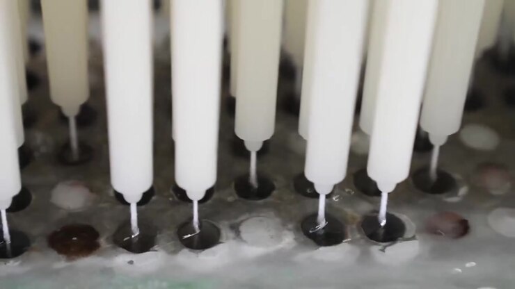 Close-up of tapered candle tips standing upright on a metal mold rack at a factory