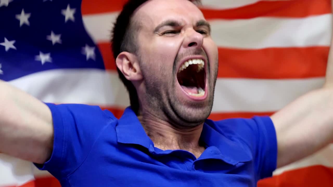 fanático estadounidense celebrando mientras sostiene la bandera de américa en cámara lenta, 4k, de alta calidad
