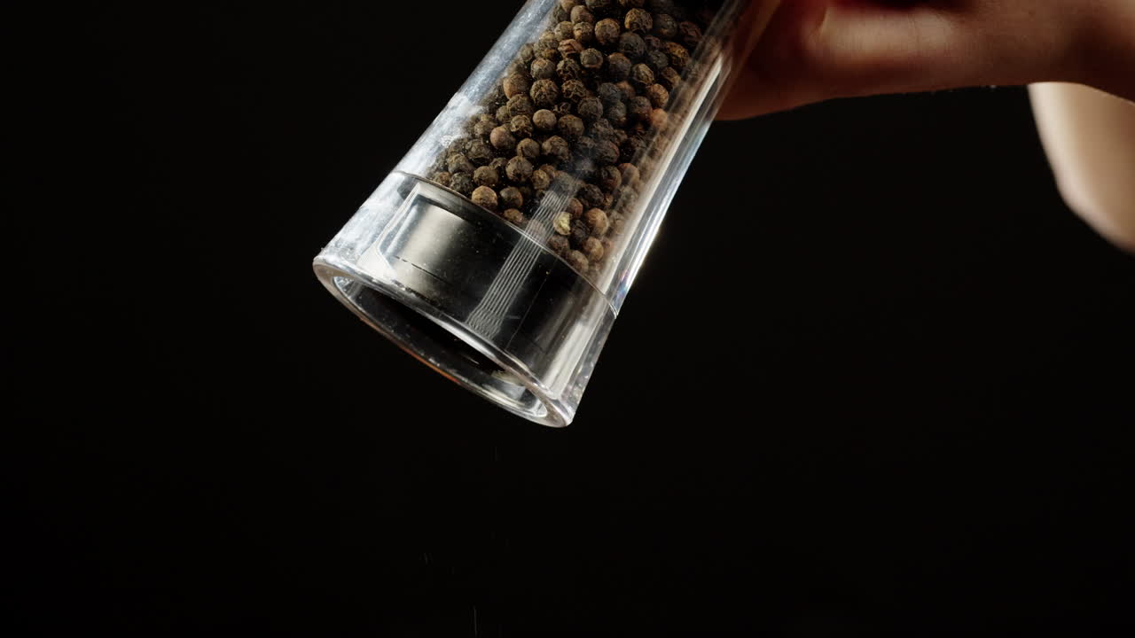 Mano moliendo granos de pimienta negra de un molinillo de pimienta