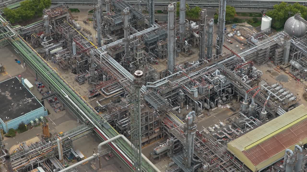 Paesaggio industriale che mostra una vasta raffineria di petrolio con intricati oleodotti e serbatoi di stoccaggio. Prospettiva aerea di un grande impianto chimico.