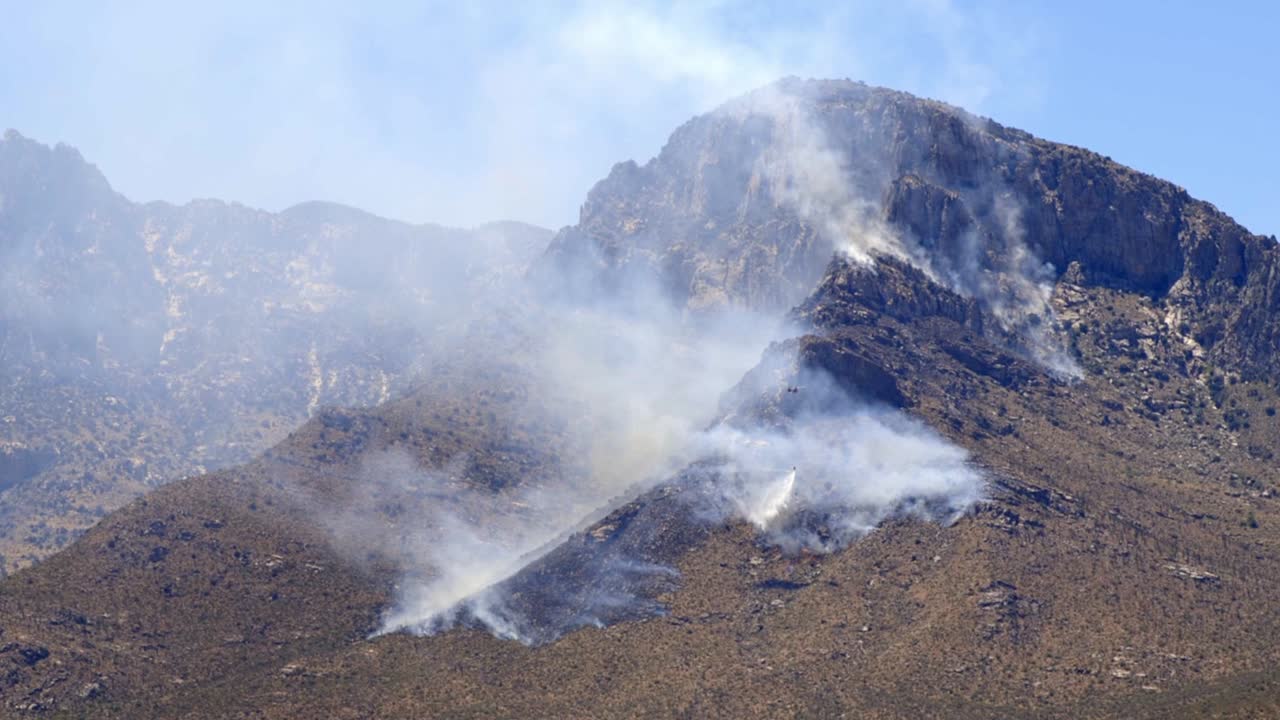 산불 연기와 애리조나 주 산타 카탈리나 산맥의 언덕 위를 비행하는 소방관 부서의 헬리콥터