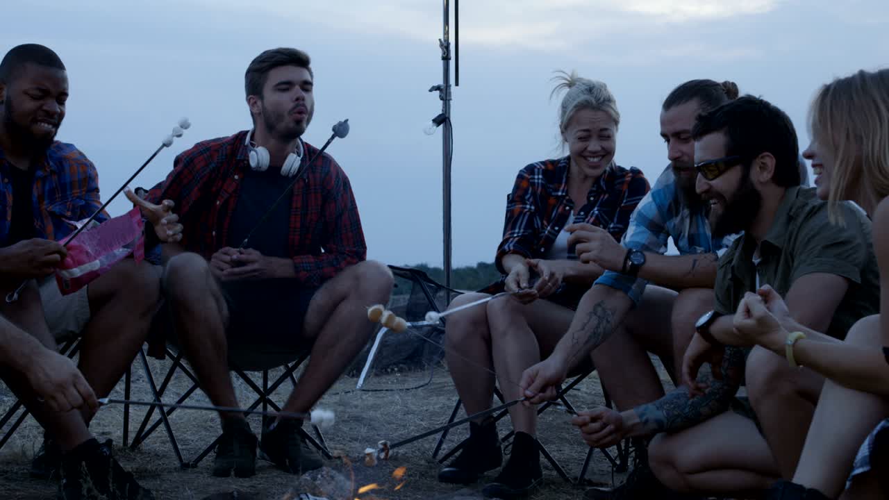 Tourists frying marshmallows at camping bonfire