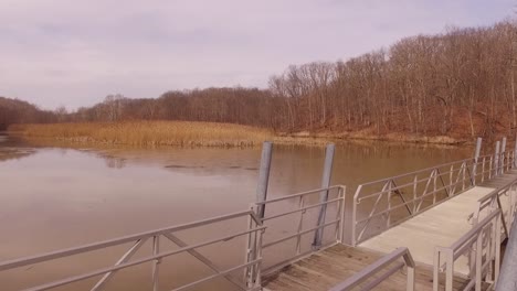 Imágenes-Aéreas-De-Un-Puente-Peatonal-Que-Cruza-Un-Lago-Helado-Durante-El-Invierno-En-Un-Parque-Estatal