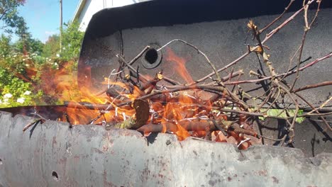 burning branches in barbecue while fire is being blown by breeze