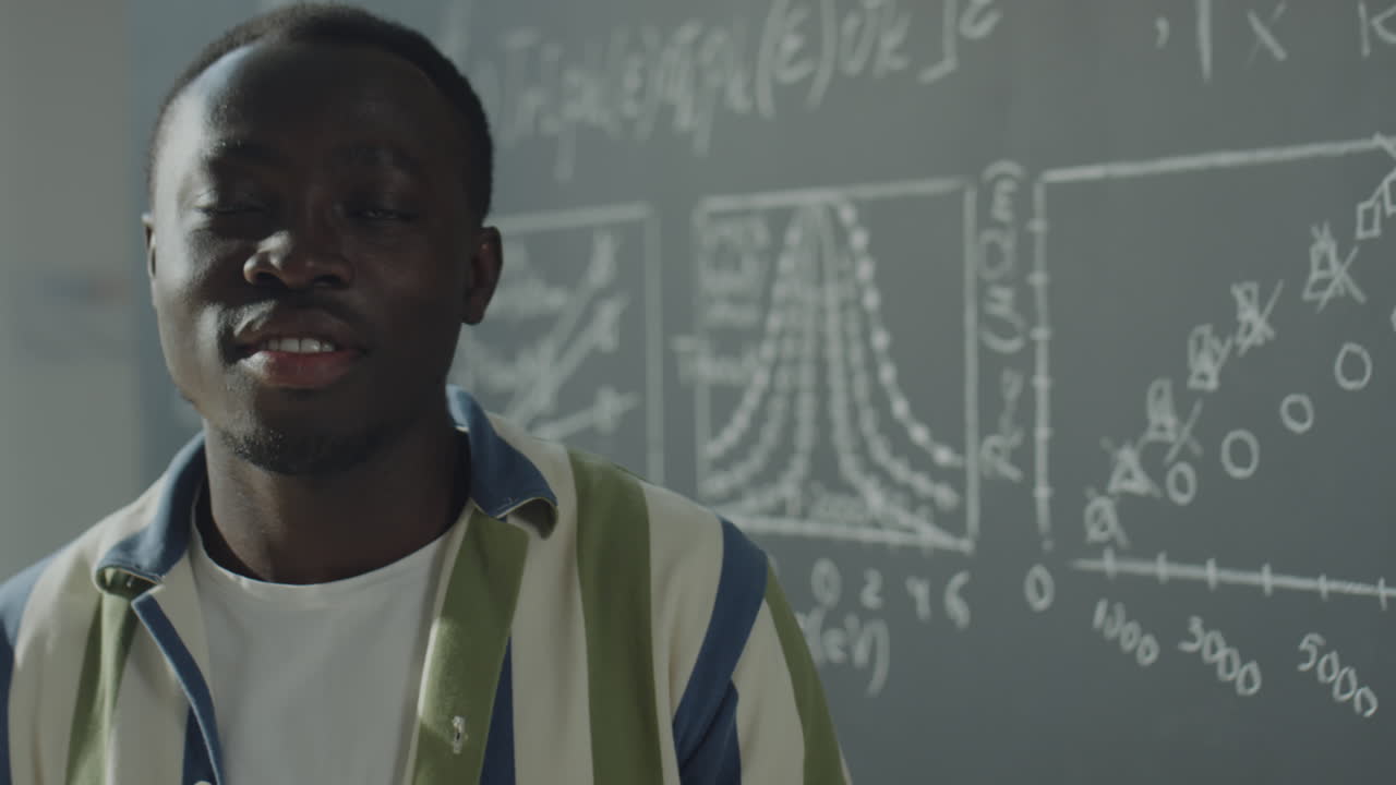 A young man standing in front of a chalkboard with mathematical equations and graphs