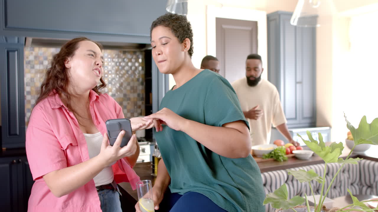 diverse friends laughing and sharing moment while looking at smartphone in kitchen