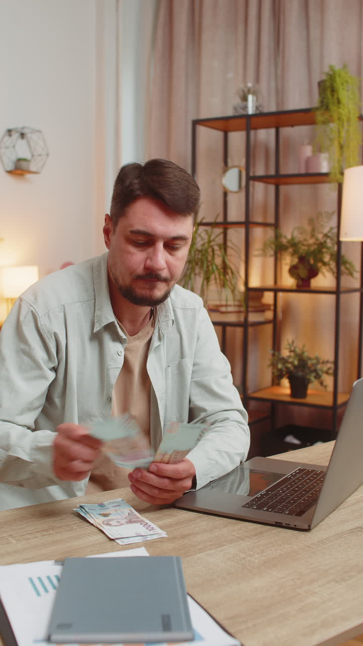 Rich happy caucasian man counting money cash using laptop calculate domestic bills at home table