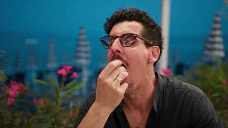 man eating a burger and smiling at the resort with sea background