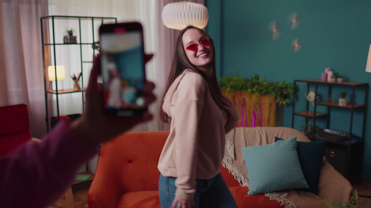 blogger adolescente alegre bailando en la cámara filmando video usando el teléfono móvil en casa en la sala de estar