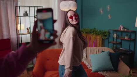 blogger adolescente alegre bailando en la cámara filmando video usando el teléfono móvil en casa en la sala de estar