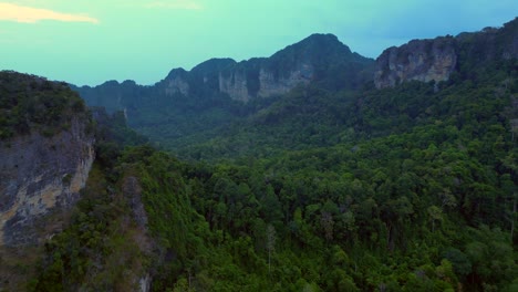 limestone cliffs and lush tropical jungle of railay beach, krabi, thailand, at dusk, creating a dramatic and serene landscape. smooth aerial view flight fly reverse drone