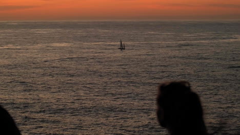 silhouette of people enjoying sunset and calm ocean with lonely sailing boat