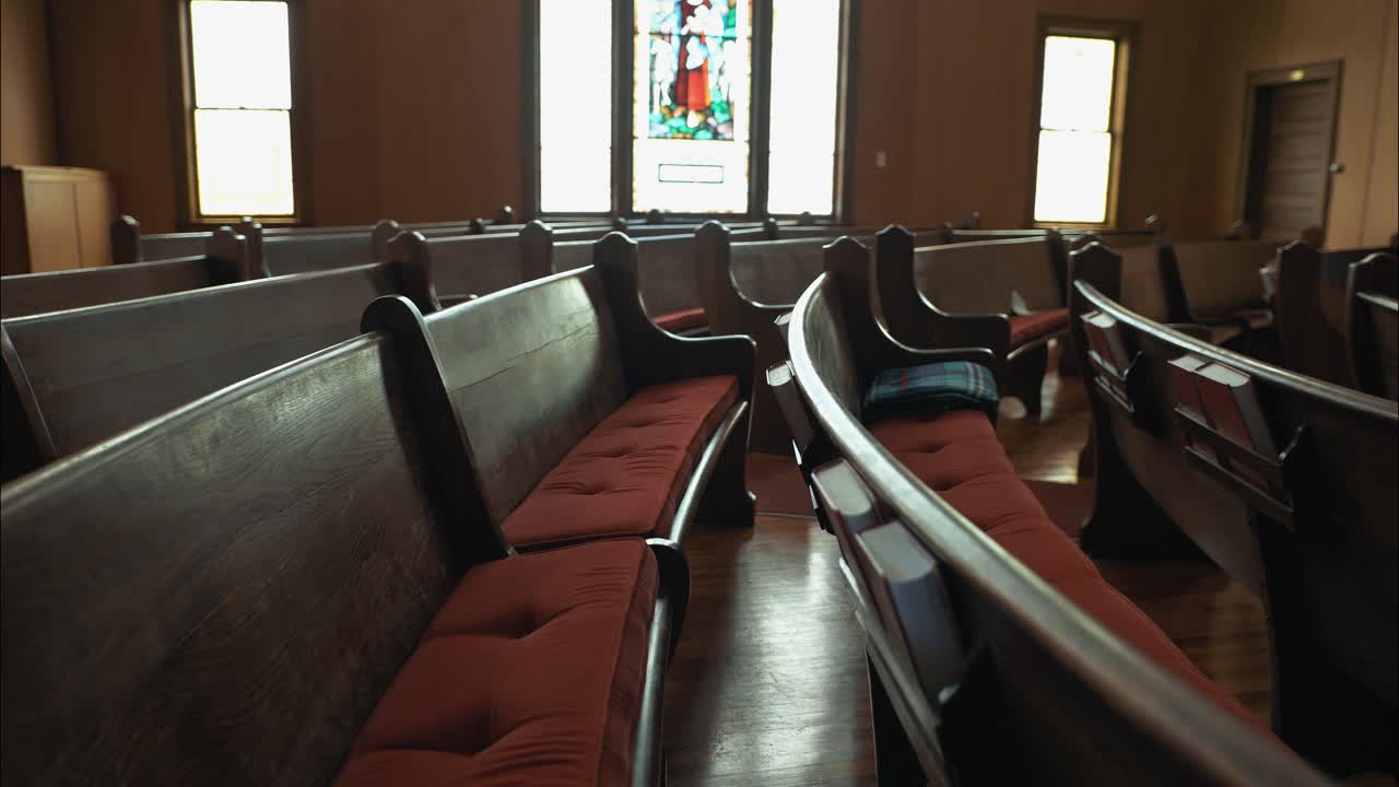 Cinematic view of an empty church interior, featuring soft light, wooden pews, and a stained-glass window of Jesus with sheep