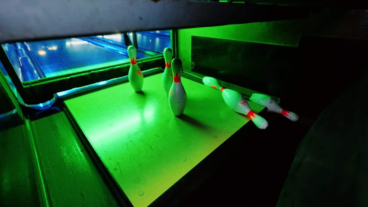 Pista de boliche iluminada em verde de um ângulo raro mostra o impacto dramático e os pinos restantes