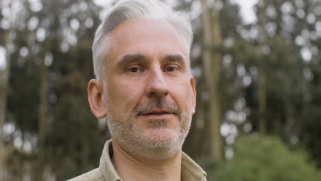 retrato de un hombre de cabello gris parado en el parque y mirando a la cámara 1