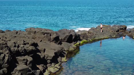 HD-Hawaii-Kauai-slow-motion-pan-left-to-right-of-Queen's-Bath-pool-with-a-person-looking-frame-left-at-ocean-view-and-a-person-in-pool