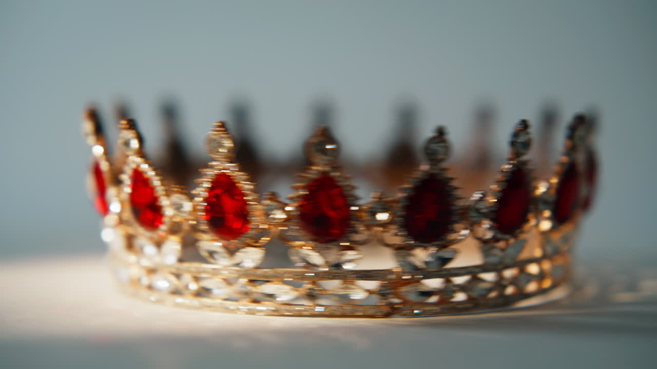 Closeup jeweled crown resting on flat surface. Red stones reflect daylight