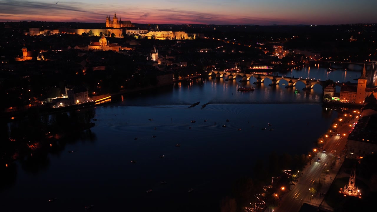 Vista aerea ad alta quota del Castello di Praga, del Ponte Carlo e del fiume Moldava al crepuscolo con un cielo al tramonto rosa e arancione luminoso, Praga, Repubblica Ceca