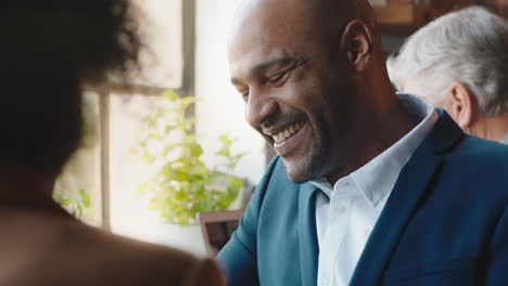 Hombre-De-Negocios-De-Raza-Mixta-Charlando-Con-Un-Colega-Que-Trabaja-En-Una-Cafetería-Compartiendo-Ideas-Disfrutando-Colaborando-En-Una-Cafetería-Ocupada-Durante-El-Almuerzo