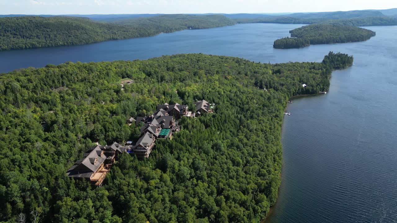 Højt droneskud over Hotel Sacacomie resorts bygninger omgivet af skov og søbred, luftfoto
