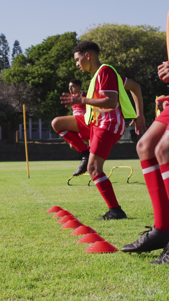 Vertical video of biracial football player on field kicking ball