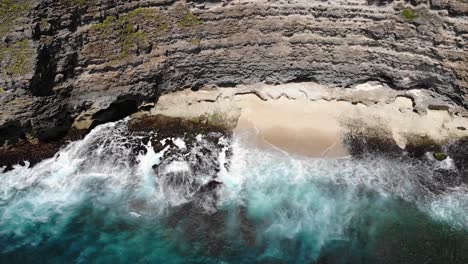 Vista-Aérea-De-Las-Olas-Rodando-Hacia-La-Playa-Debajo-De-Un-Acantilado-En-Uluwatu,-Bali