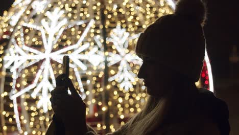 woman taking pictures with a phone of a christmas lights at night