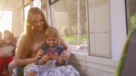 woman and daughter using mobile phone internet social network application, traveling by bus or tram