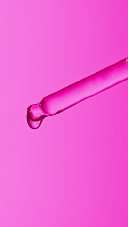 close-up of a glass dropper with a drop of pink liquid