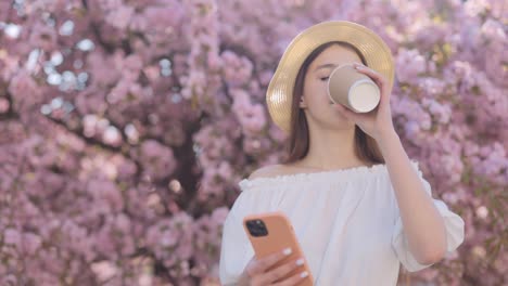 teenager drinking coffee and using phone under cherry blossom trees