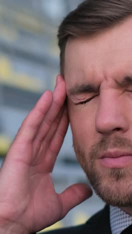the man is holding his hand to his temple due to a headache, which causes discomfort in the muscle of his forehead.