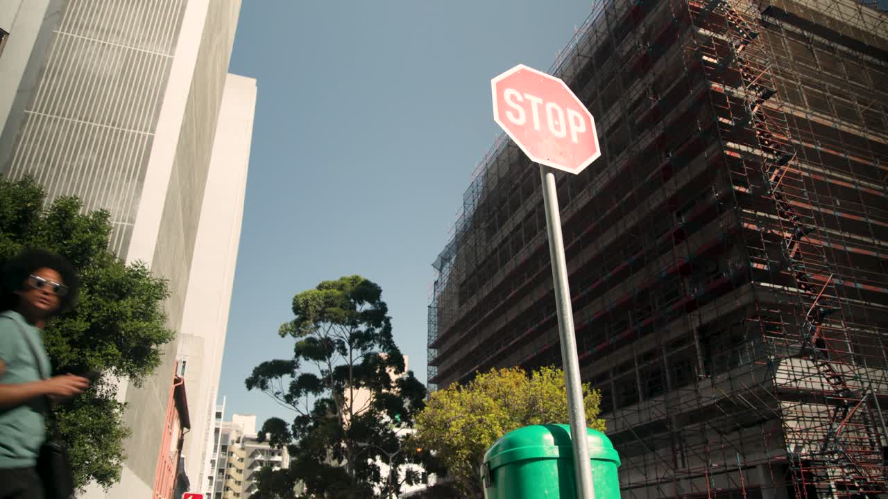 La señal de STOP y los contenedores permanecen fijos mientras los peatones entran y cruzan la calle.