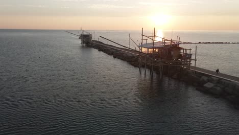 Aerial-panoramic-landscape-view-of-a-trabucco-silhouette,-a-traditional-fishing-machine,-on-the-italian-seashore,-at-sunset