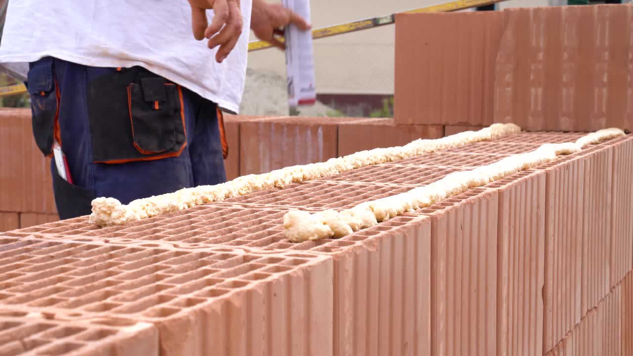 Worker applying adhesive foam onto ceramic blocks for brick wall
