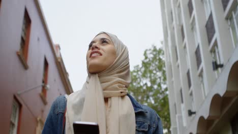 mujer en hijab usando teléfono móvil mientras camina por la calle 4k