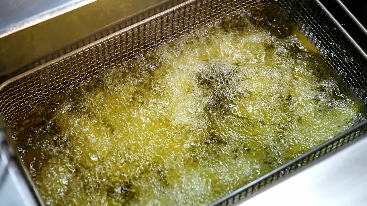Pommes frites i frituregryden. Fastfoodrestaurant, tilberedning af kartofler, sprøde fritter. Junkfood-koncept. Video fra oven. Nærbillede